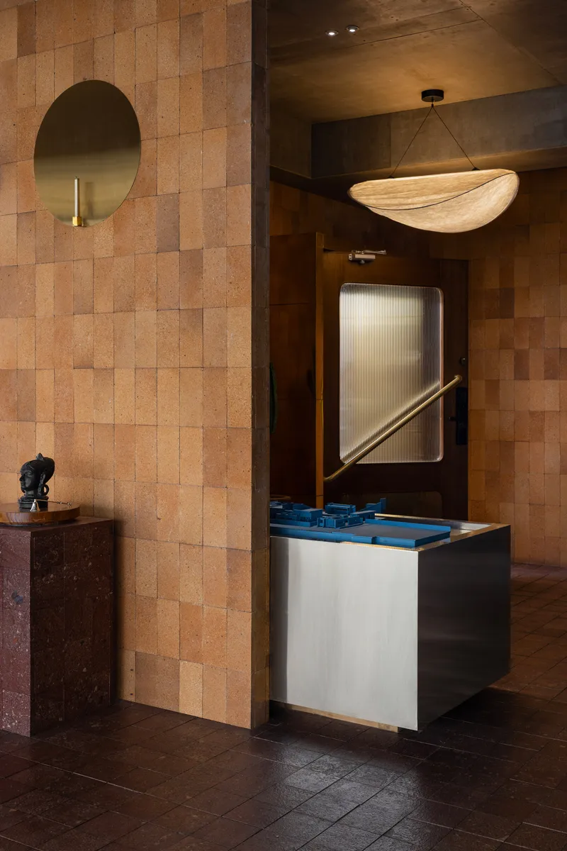 Entry nook with cork tile wall, circular mirror, and illuminated reception desk under pendant fixture