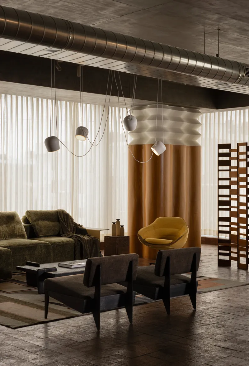 Interior lounge with exposed spiral ductwork overhead and pendant lights suspended by draped cables