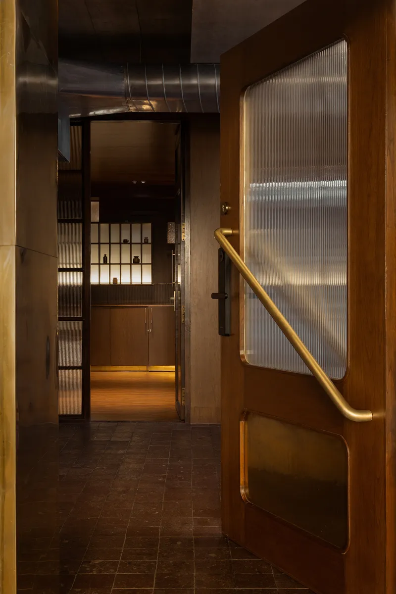 Passageway with brass handrail on timber-framed door leading to glass partitions and cabinetry beyond