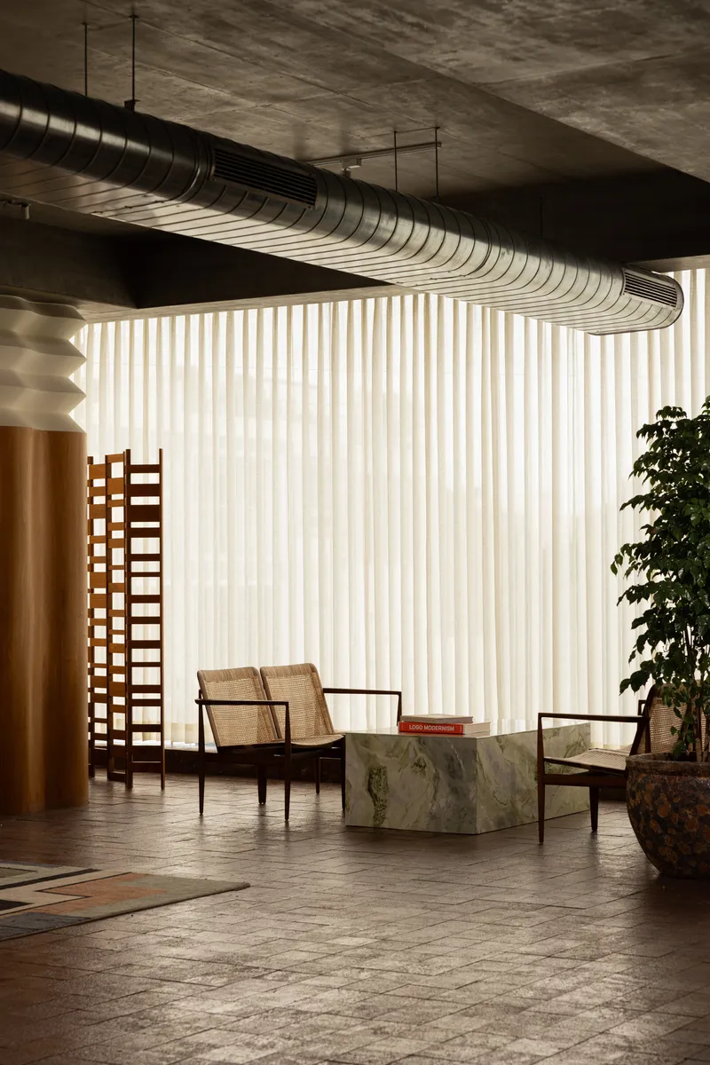 Interior seating area with exposed spiral ductwork overhead and vertical fabric curtain filtering natural light