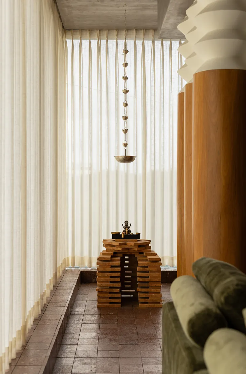 Narrow passage with vertical curtain wall and tiered timber altar beneath a suspended brass pendant