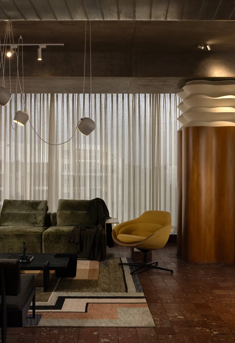 Lounge area with suspended geometric pendant lights and exposed concrete ceiling in evening illumination