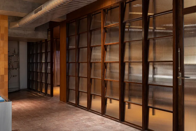 Sliding timber-framed glass partition wall with reeded glazing panels and exposed mechanical ductwork above