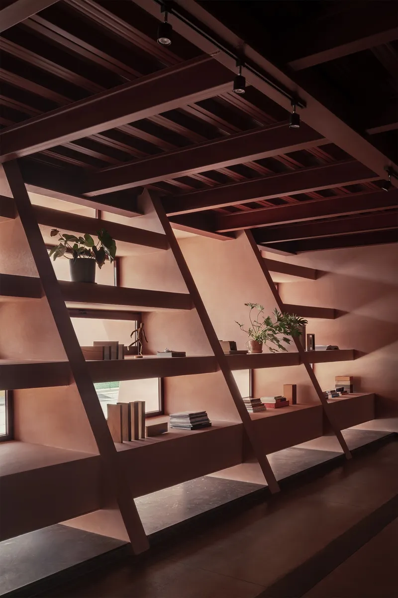 Angled steel shelving with books and plants below an exposed beam ceiling in warm light