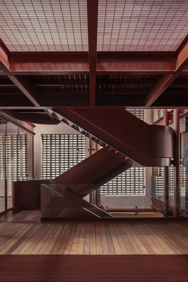 Central steel staircase with timber treads against a perforated block screen wall under exposed beams