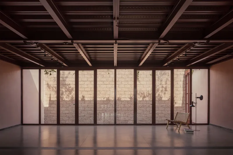 Gallery room with exposed timber joists and perforated block window wall with a single chair