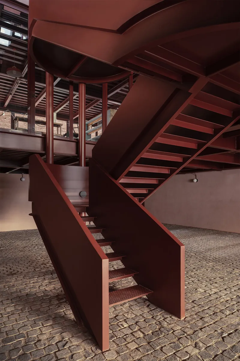 Multi-level steel staircase with solid balustrades over cobblestone flooring and cylindrical columns