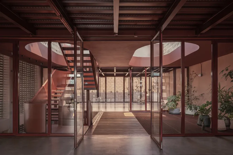 Glass-partitioned corridor with steel frame doors looking toward a spiral staircase