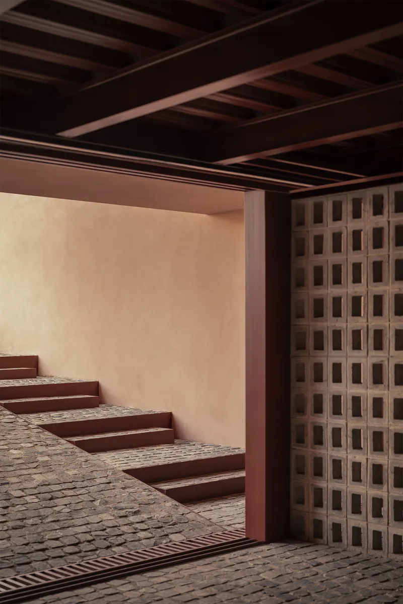Steel-framed doorway opening to a courtyard with cobblestone paving and perforated brick screen