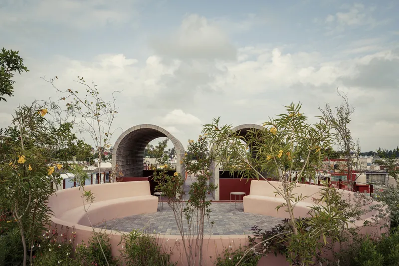 Rooftop terrace with pink curved seating walls and twin barrel vault arches framed by planted beds under cloudy skies
