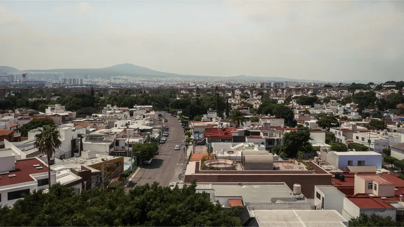 Wide aerial view of low-rise residential rooftops with mountains visible on the horizon under hazy afternoon light