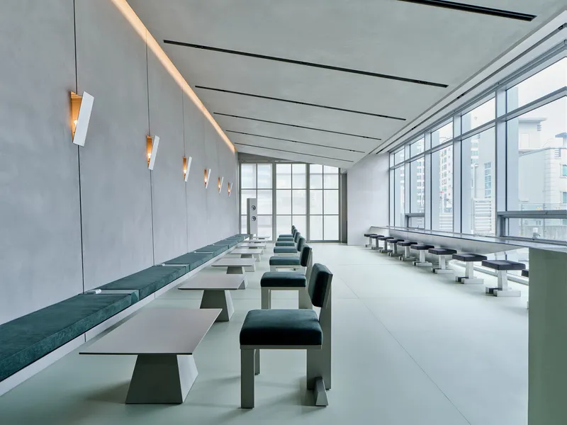 Long room with white tables flanked by teal seating under a coved ceiling with linear recessed lighting