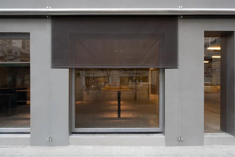 Street facade with gray metal panels and retractable mesh screens above the glazed storefront opening
