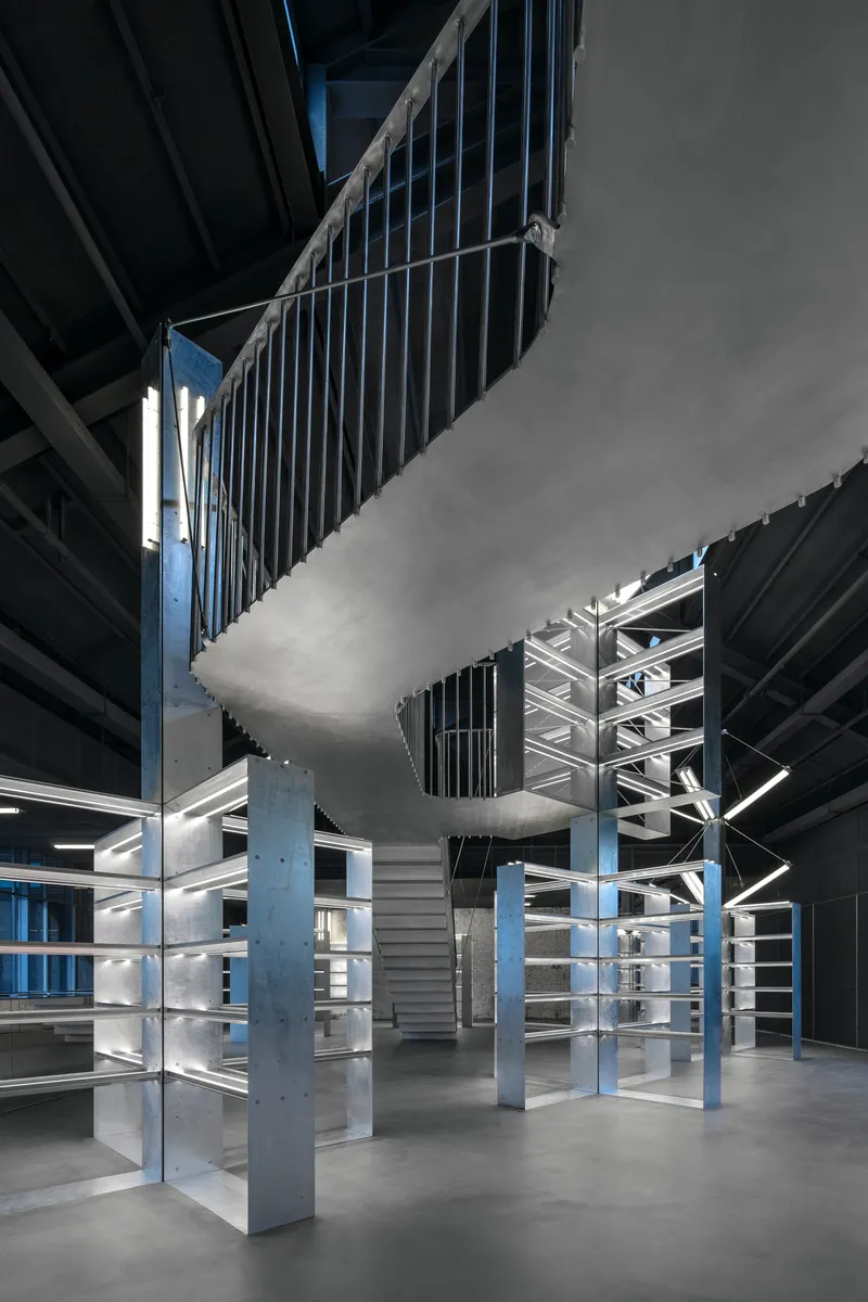 Interior view of the double-height space with vertical metal slat screens and blue steel columns