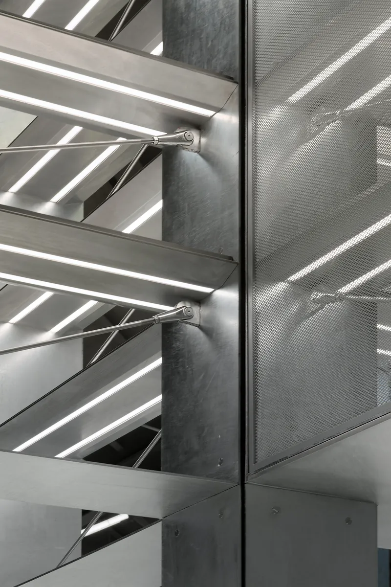 Detail of perforated metal panel meeting steel shelf supports at a concrete column