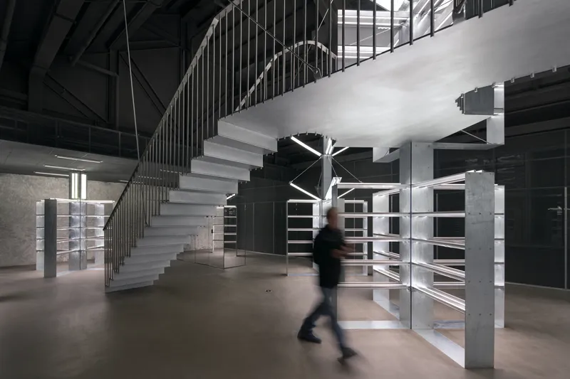 Concrete staircase with vertical metal balustrade and a figure crossing the polished floor below