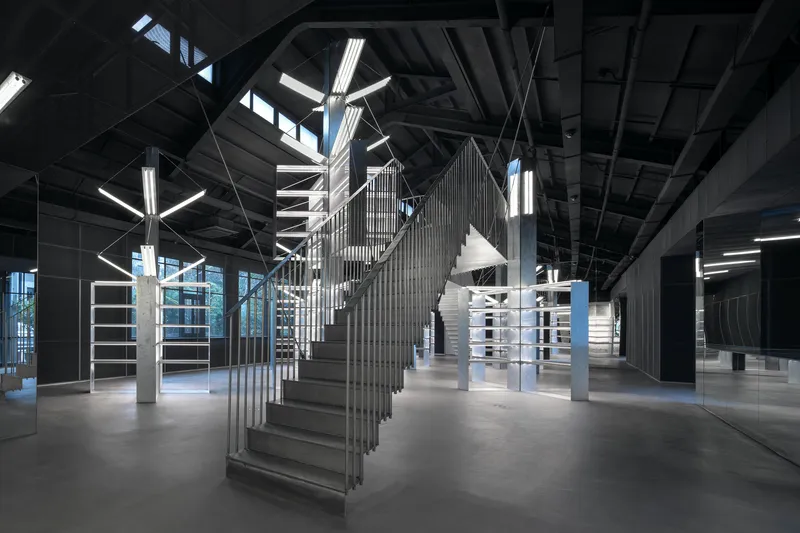 Sculptural staircase with vertical slat balustrade beneath exposed black ceiling structure and linear lighting
