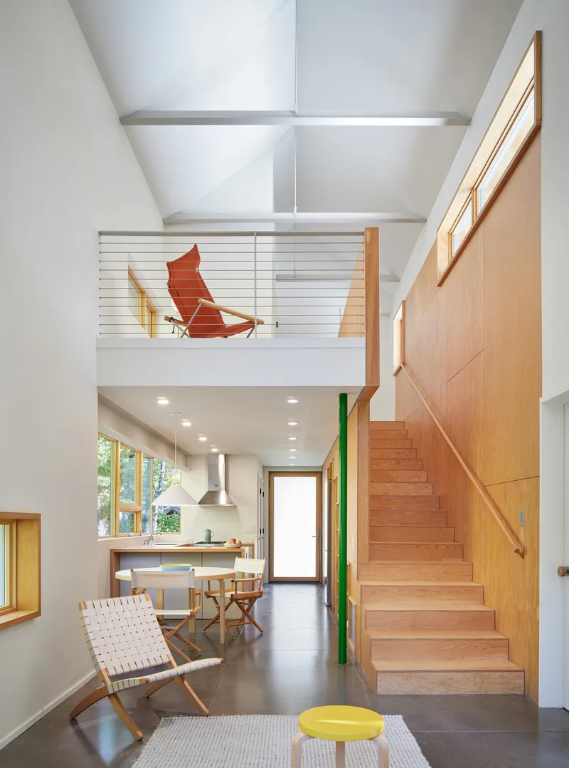Double-height interior with exposed ceiling beams and timber staircase leading to a mezzanine with cable railing