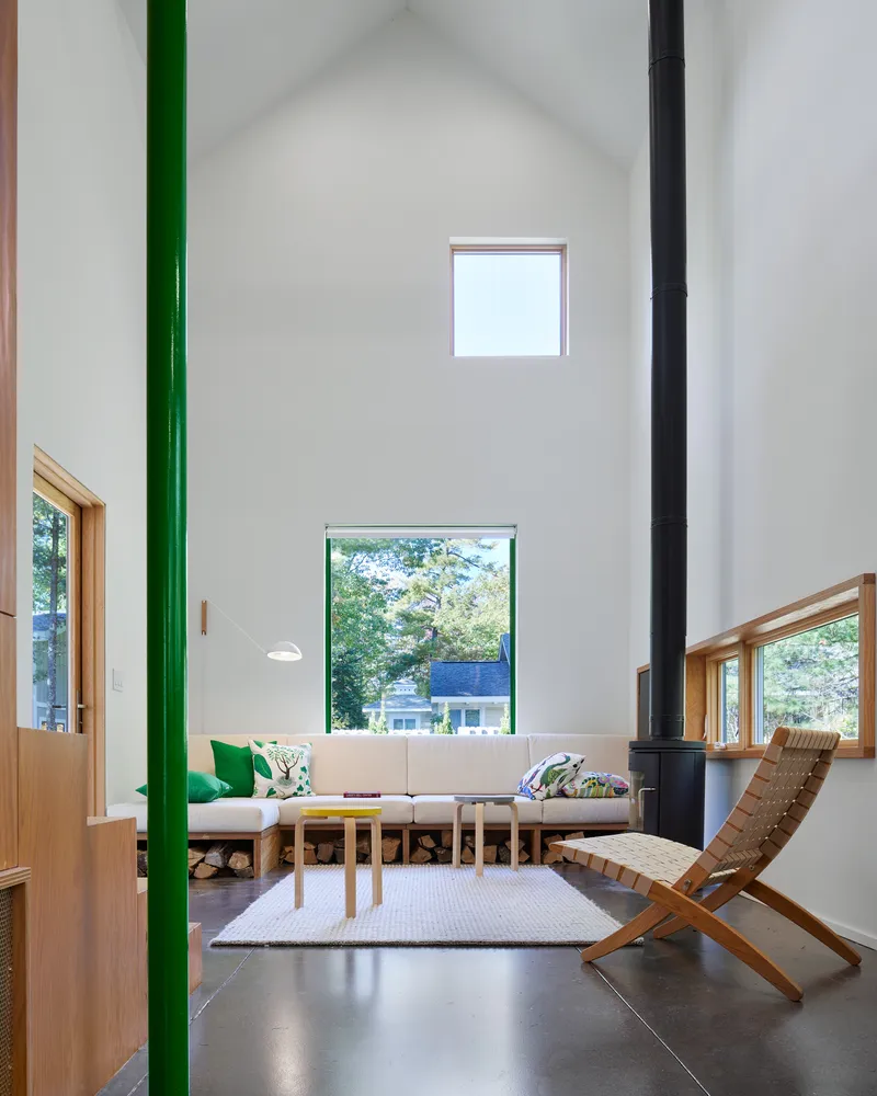 Living room with exposed green steel column and black woodstove beneath a vaulted white ceiling
