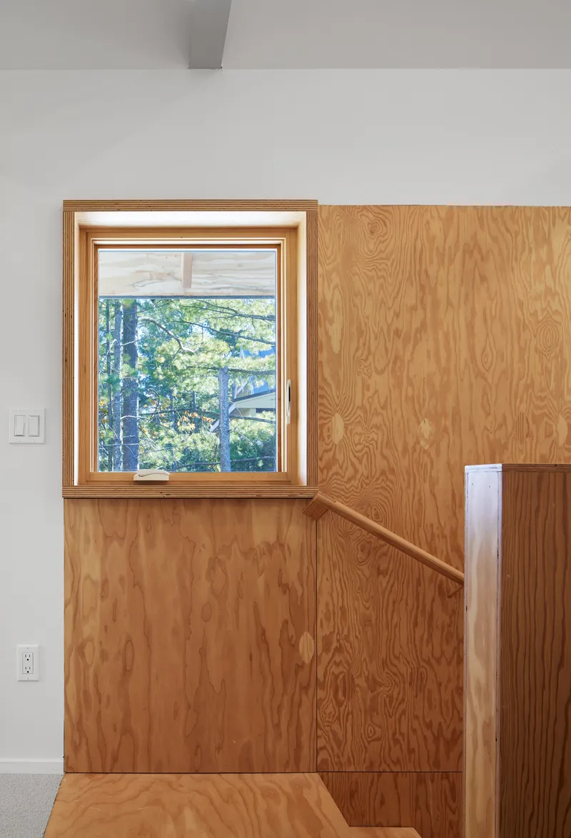 Interior corner with oak plywood wall paneling and recessed staircase railing beneath a picture window