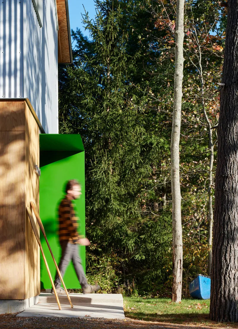 Entrance threshold with bright green interior wall framed by plywood and corrugated metal cladding with a person walking