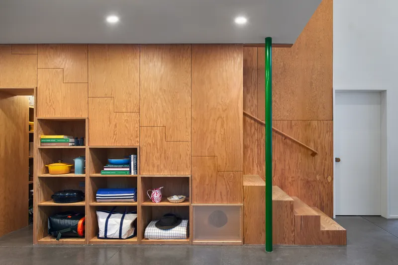Plywood storage wall with open shelving at base and staircase with green steel handrail