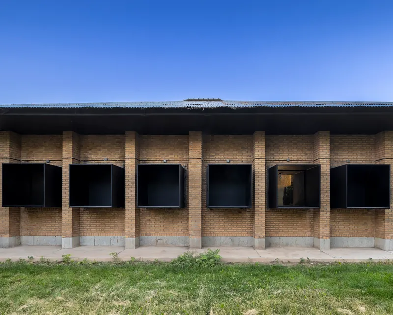 Facade with yellow brick columns and black metal-framed windows under a corrugated metal roof edge