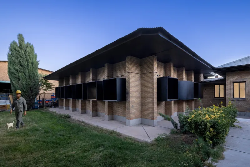 Corner of the brick building with projecting black metal window boxes at dusk with a walking figure