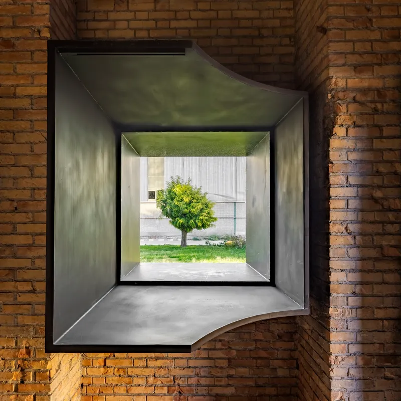 Deep window opening framing a tree in the courtyard through layered metal and concrete reveals