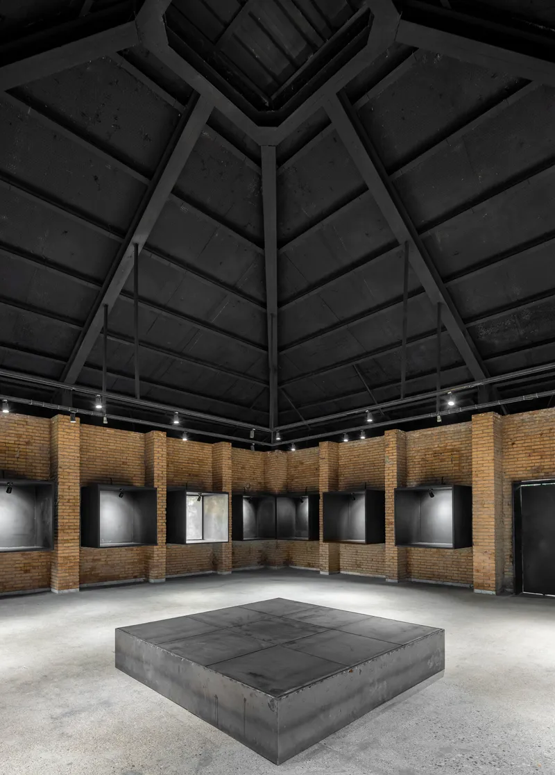 Gallery interior with pyramidal timber ceiling and brick perimeter walls illuminated by track lighting