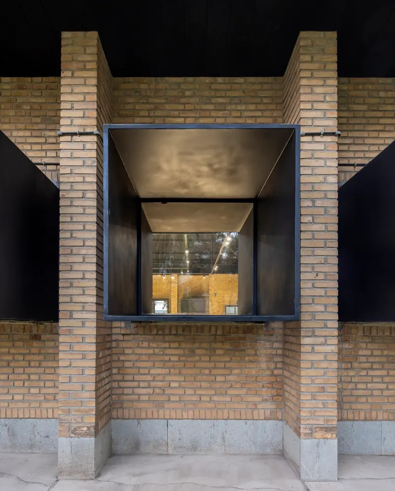 Recessed black steel window volume framed by yellow brick piers and concrete base at night