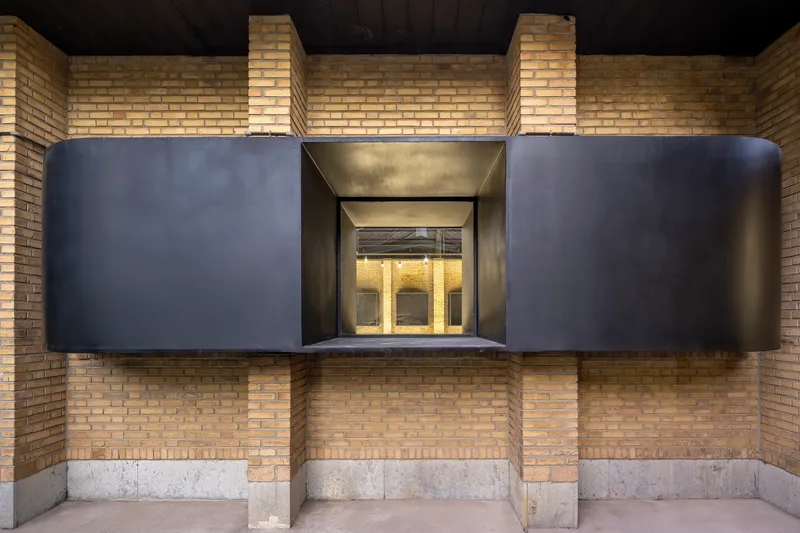 Frontal view of the projecting black steel bay window set within yellow brick courtyard walls