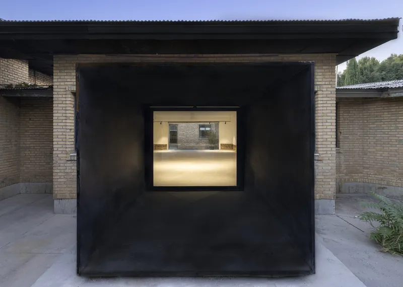 Black steel passage framing a view through to a sunlit courtyard with yellow brick walls