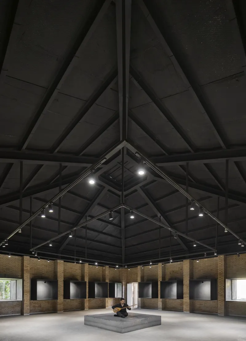 Upward view of the pyramidal timber roof structure with track lighting and concrete plinth below