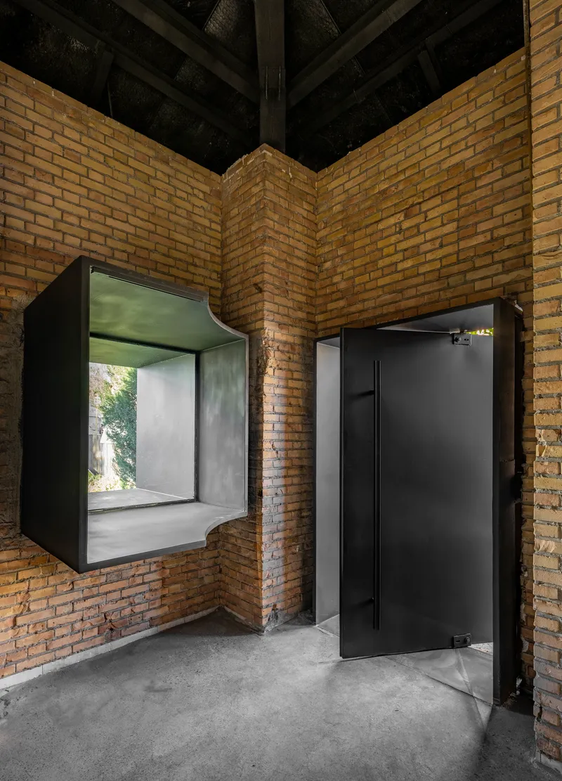 Corner courtyard with yellow brick walls, black timber ceiling and two black-framed box windows with a concrete floor