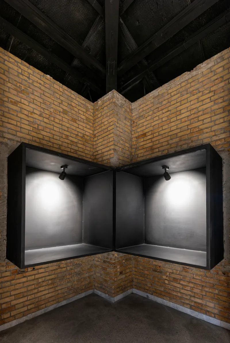 Corner display niche with black metal frame and spotlights set into yellow brick walls under exposed timber beams