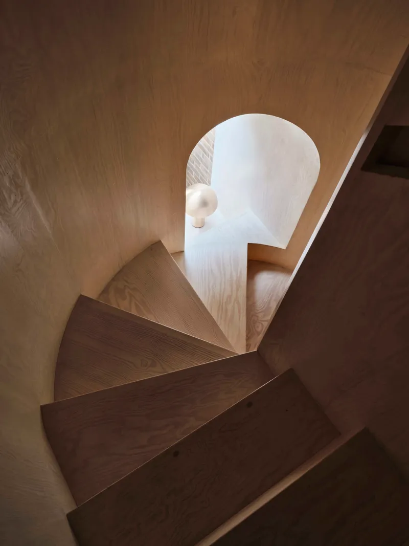 Top-down view of curved timber staircase wrapping around a white plaster wall with wooden handrail
