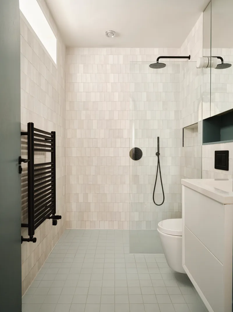 Bathroom with white square tile walls, black fixtures, towel radiator and skylight above shower area