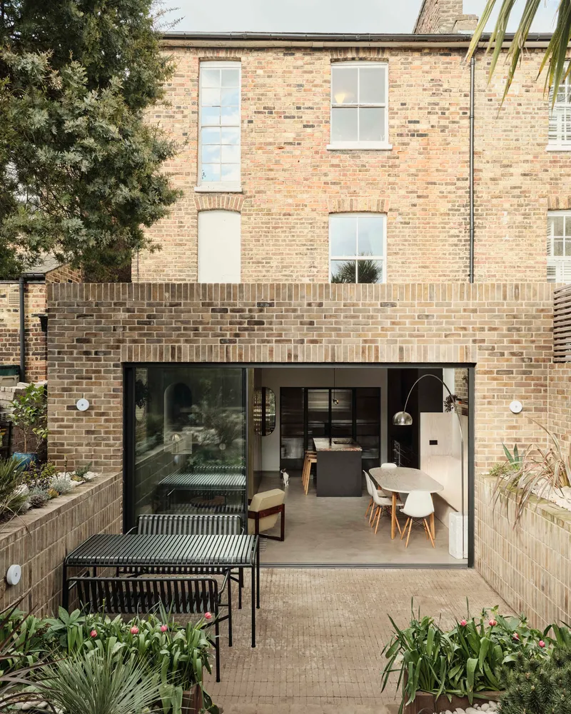 Garden view showing the rear extension with sliding glass doors beneath the original brick house