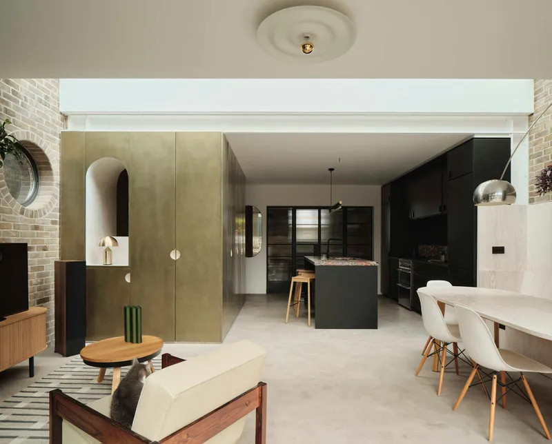 Open-plan living area with brass-clad volumes and continuous pale flooring under indirect perimeter lighting