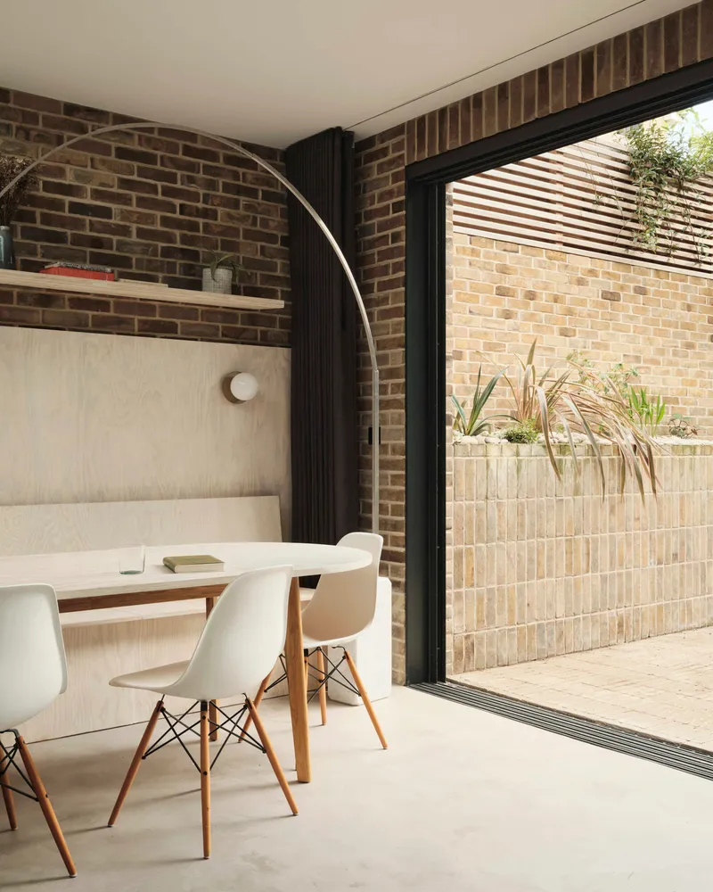 Dining area with arched brick recess and sliding glazing overlooking the courtyard planted bed