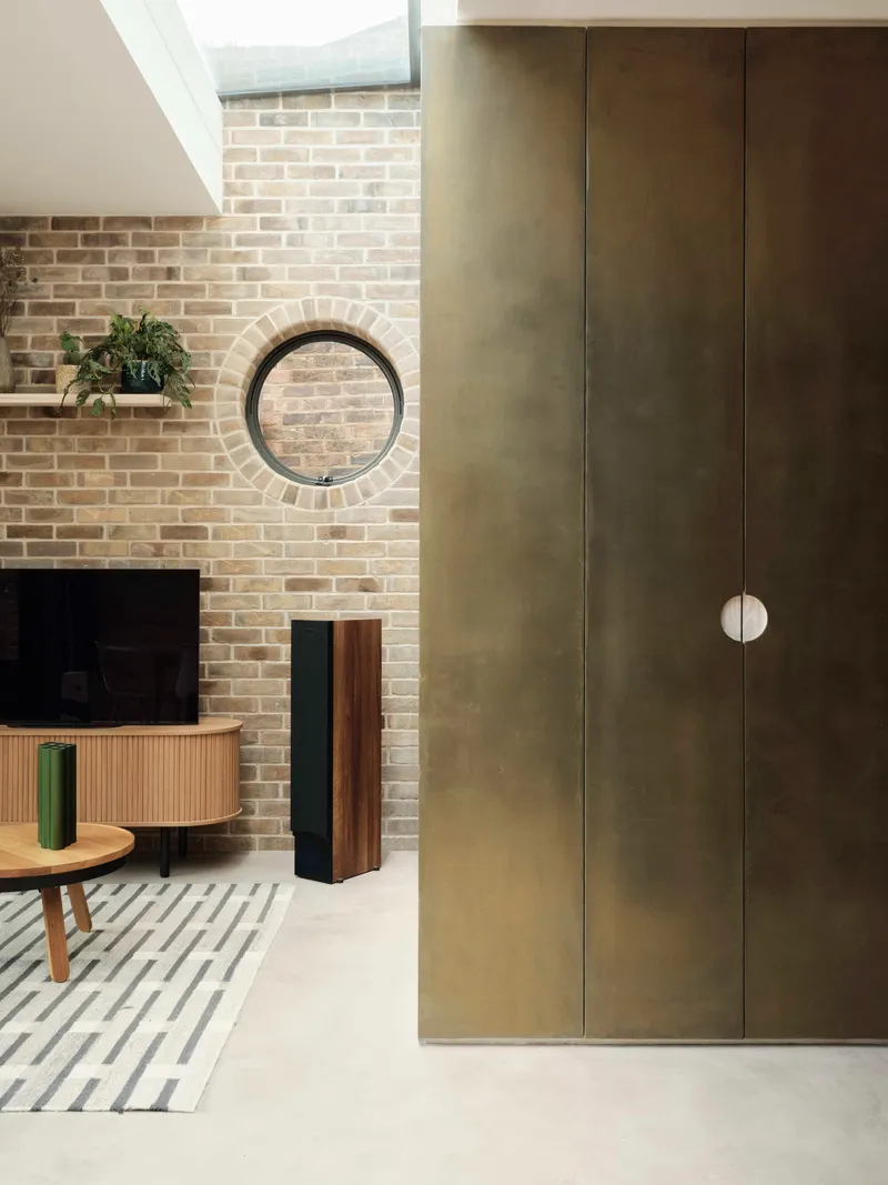 Living space showing tall brass-clad joinery beside a buff brick fireplace wall with circular window