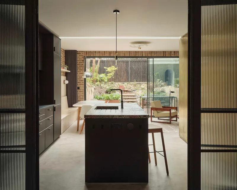 View through fluted glass doors toward kitchen island and planted rear courtyard beyond