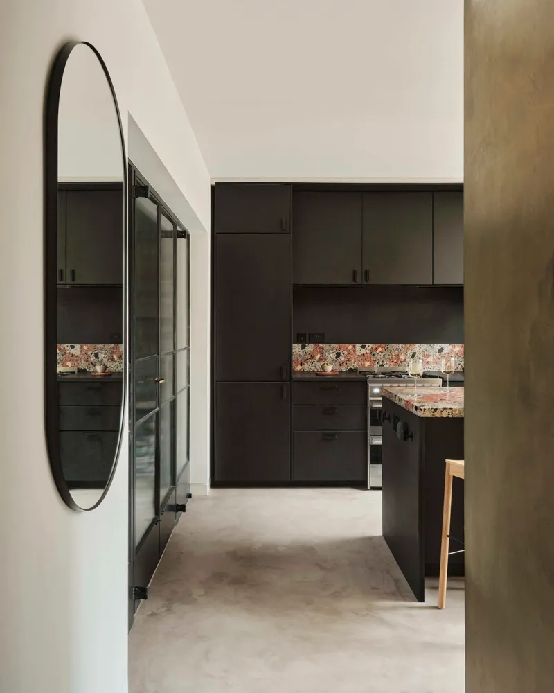 Hallway view showing oval mirror and dark joinery with multicoloured terrazzo splashback