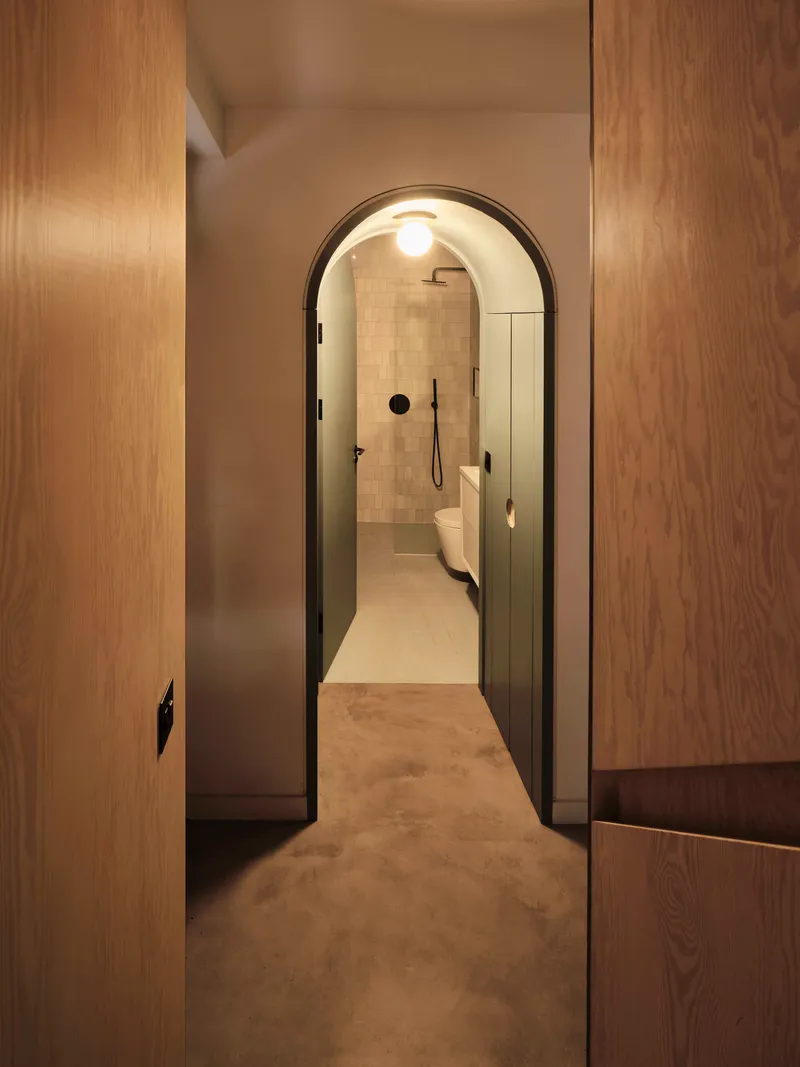 Arched doorway with black frame opening into bathroom with cream tiled walls
