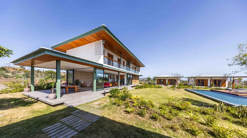 Garden view of the two-story volume with timber-lined eaves and glazed ground floor opening to lawn