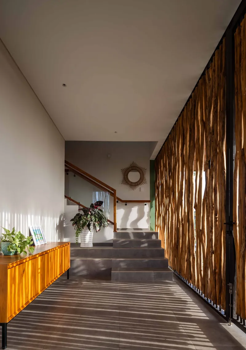 Interior staircase with vertical timber batten screen casting dappled sunlight across dark stone treads