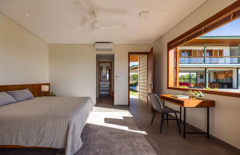 Bedroom interior with timber-framed windows overlooking courtyard and opposite wing in bright daylight