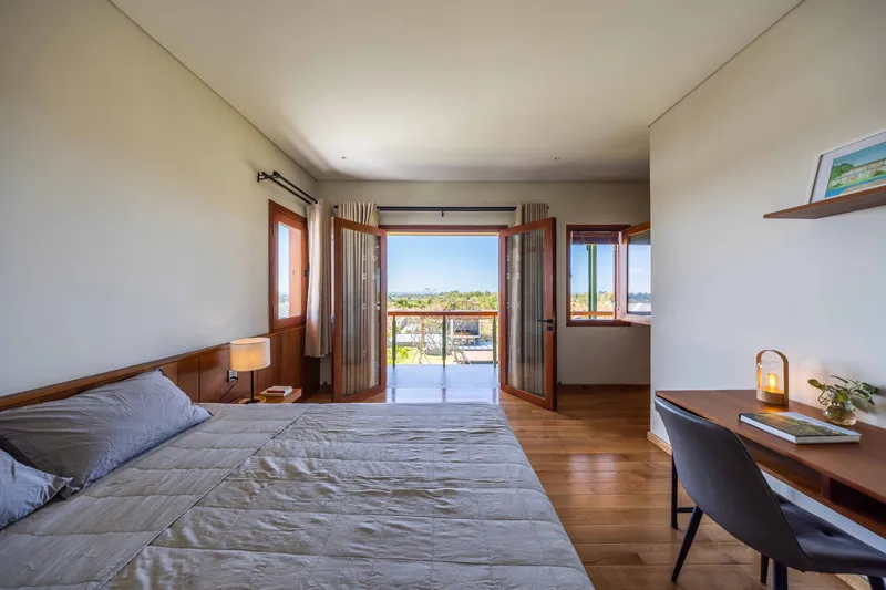 Bedroom with timber joinery opening through folding doors to balcony under clear blue sky