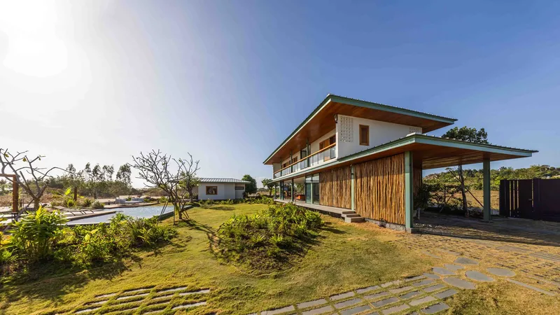 Two-storey residence with vertical bamboo cladding and open carport beside a planted lawn under clear sky
